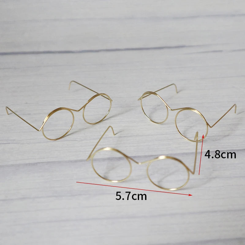A set of five metal round glasses frames displayed on a light wooden surface with dimension markings.