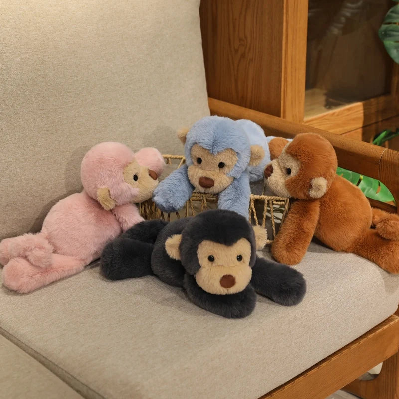 A collection of soft plush monkey toys in pink, blue, and brown colors resting on a wooden surface.