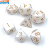 A set of seven mini polyhedral dice in white and gold colors arranged on a white surface.