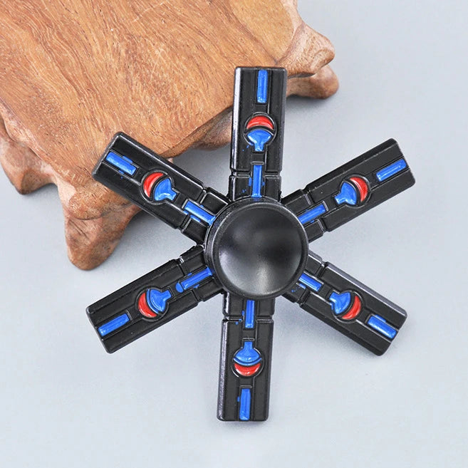 A black metal fidget spinner with a rainbow finish is held by a person's hand.