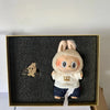 A plush toy of Labubu with large eyes and light brown fur is displayed in a gold frame.