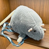 A gray mouse plush toy with light pink ears and a blue strap is shown resting on a wooden surface.