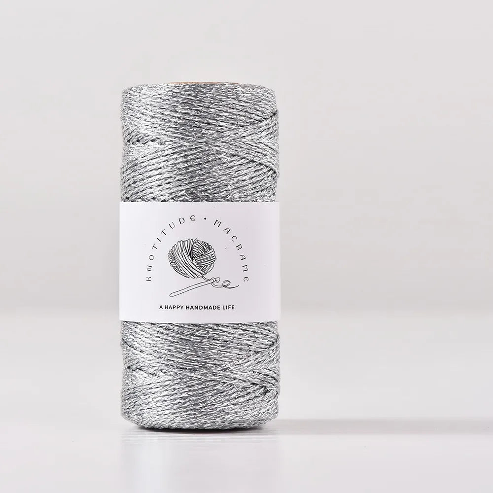 A spool of metallic gray yarn for knitting and crochet with a white label featuring the brand name and a happy handmade life 