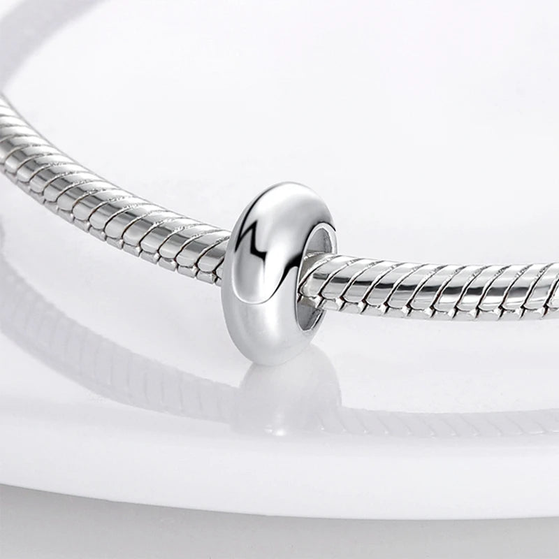 A silver charm bead is shown attached to a flexible silver chain, ready for DIY bracelet making.