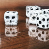 A set of white skull dice, used for Halloween and party games, are displayed on a wooden surface.