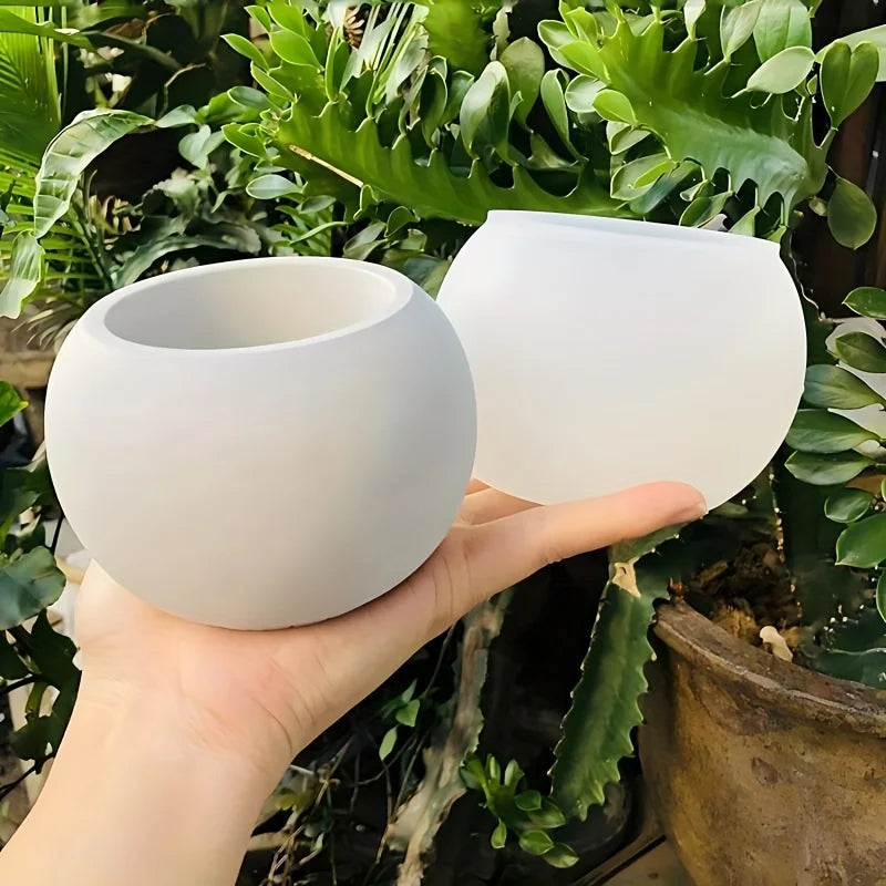 A hand holds a white silicone round pot mold, surrounded by green foliage.