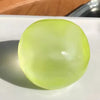 A smooth, translucent lime green squeezy ball resting on a white surface.