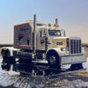 A silver Peterbilt 389 diecast truck model with lights and sound parked on a wet surface.
