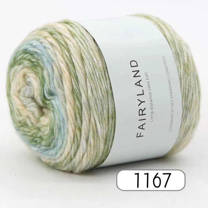 Spool of Fairyland long distance cake ball yarn in a gradient mix of green, blue, and cream.