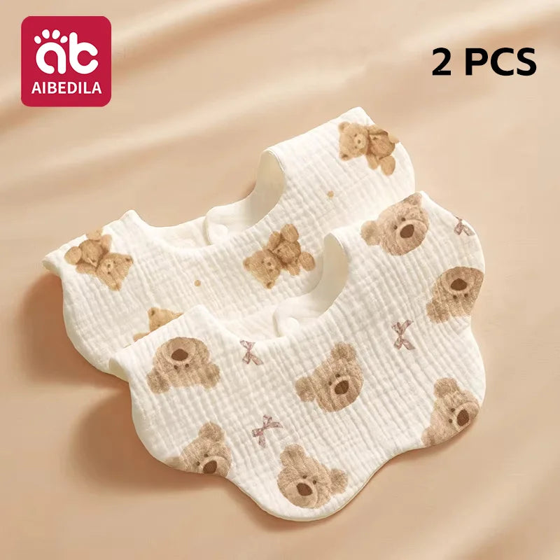 Two pairs of white cotton gauze baby bandana bibs with brown bear patterns shown on a beige background.