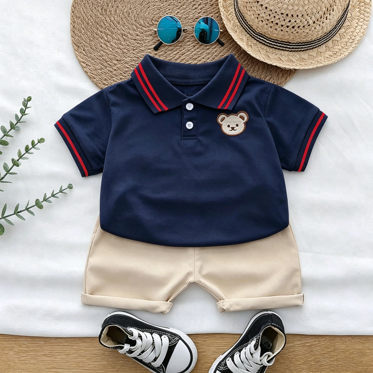 A navy blue polo shirt and beige shorts set for a toddler, featuring an embroidered bear on the chest.