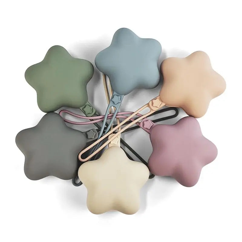 A set of five soft, star-shaped pacifiers and teethers in various muted pastel colors attached to a strap.