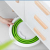 A hand is holding a bright green collapsible bucket with a white lid next to a white cabinet.