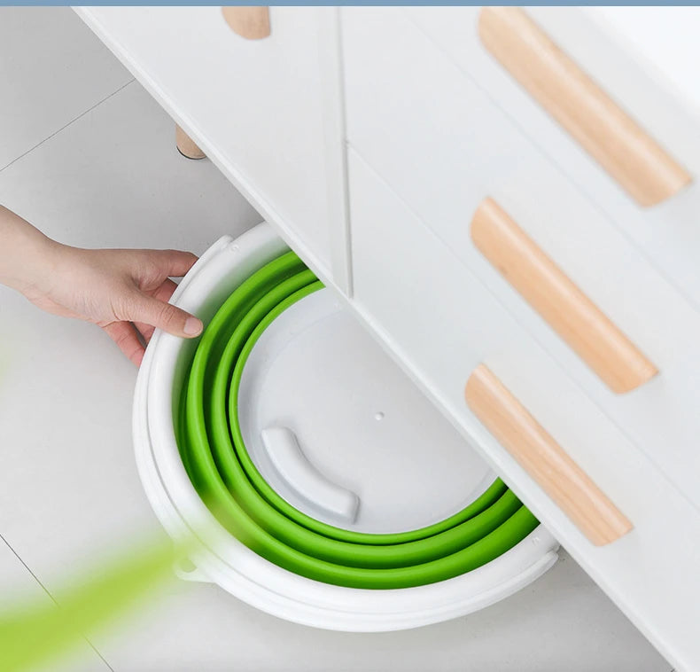A hand is holding a bright green collapsible bucket with a white lid next to a white cabinet.