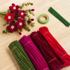 A collection of 400 chenille stems in mixed colors, including red, magenta, and green, laid out on a wooden surface.