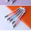 A collection of dual-ended silicone nail art dotting pens with crystal handles in various colors resting on an orange book.