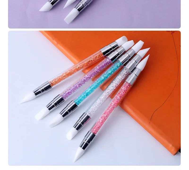 A collection of dual-ended silicone nail art dotting pens with crystal handles in various colors resting on an orange book.