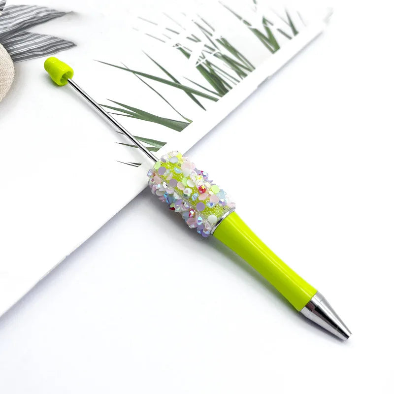 A bright lime green ballpoint pen with a sparkly, multicolored sequin bead on the tip, resting on white paper.