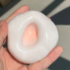 A hand holds a white, squishy stress relief ball with a translucent pink center.