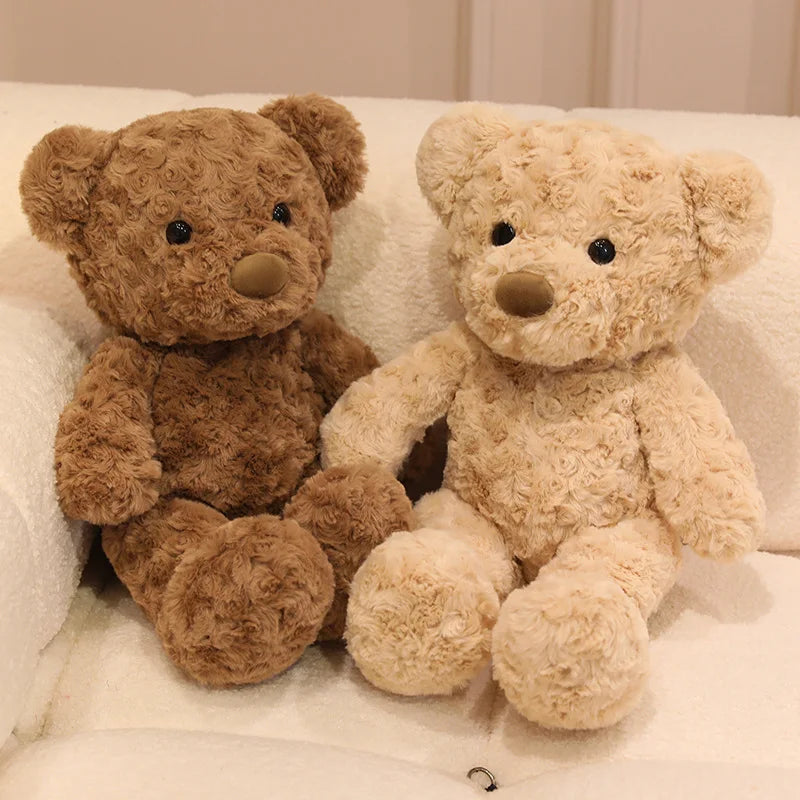 A pair of soft, fluffy teddy bear plush toys in brown and cream colors sitting on a white surface.