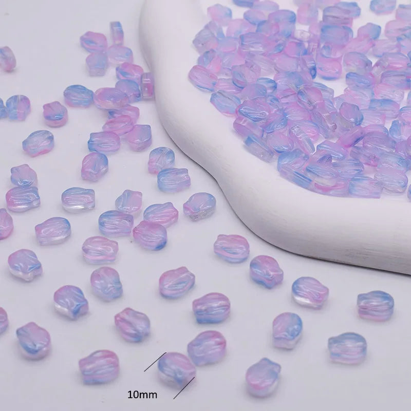 A pile of iridescent purple and blue gradient glass beads is shown next to a white ceramic tool.