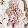 A baby wearing a knitted outfit and hat is holding a silicone teether toy shaped like a cartoon car.