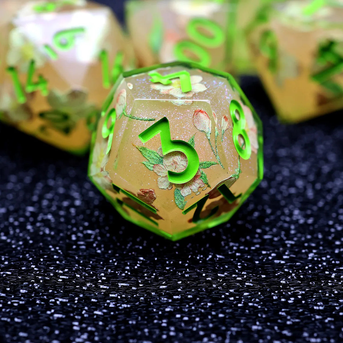 A close-up of a green resin polyhedral dice set with numbers and floral designs resting on a dark surface.