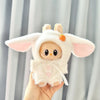 A white long-eared rabbit costume for a 17cm Labubu doll with pink accents being held by a hand.
