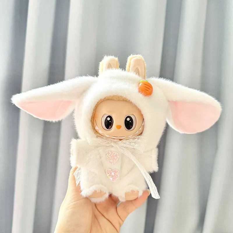 A white long-eared rabbit costume for a 17cm Labubu doll with pink accents being held by a hand.
