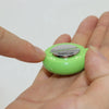 A hand is holding a small, lime green electric shock buzzer toy with a silver switch.