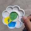 A white flower-shaped disposable paint palette with various colored paints inside, held by a hand.