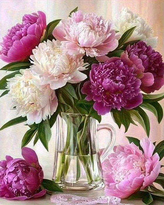 A bouquet of pink and purple peonies and roses arranged in a glass vase on a white surface.