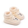 A pair of handmade knitted baby booties shaped like a lion, light beige color.