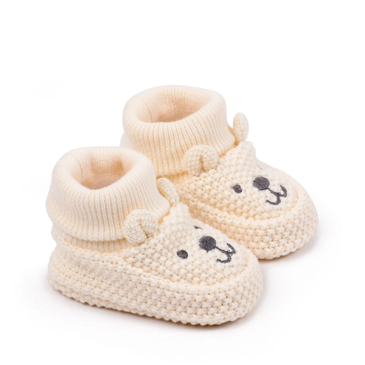 A pair of handmade knitted baby booties shaped like a lion, light beige color.
