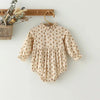 A vintage floral baby girl outfit set featuring a blouse and romper hanging on a wooden rack.