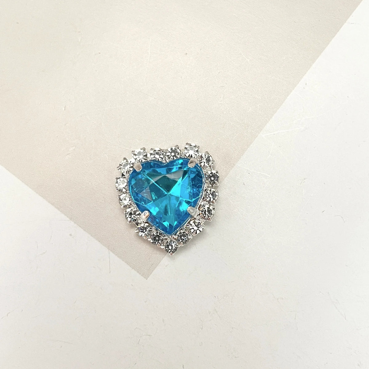 A brilliant blue heart-shaped gemstone surrounded by clear rhinestones for DIY crafts.