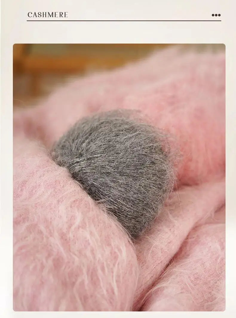 Close-up of fluffy pink cashmere yarn with a tuft of gray fiber resting on the surface.