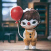 A small mischievous figure from the POP MART Hirono series with brown hair and large white eyes holding a red balloon.