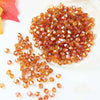 A pile of small, faceted amber and orange-colored crystal beads scattered on a white surface.