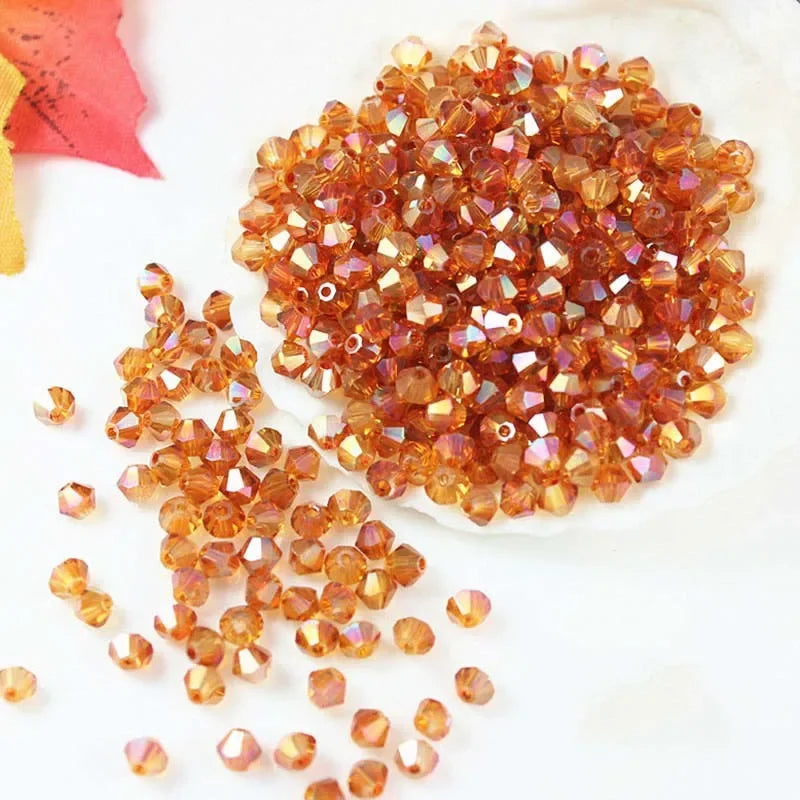 A pile of small, faceted amber and orange-colored crystal beads scattered on a white surface.