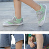A close-up of a child wearing light green and gray barefoot training sneakers on a paved surface.