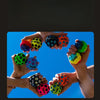 Several hands are holding and playing with colorful moon balls against a bright blue sky.