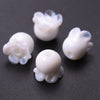 Several small, translucent white glass charm pendants shaped like lily of the valley buds are scattered on a dark surface.