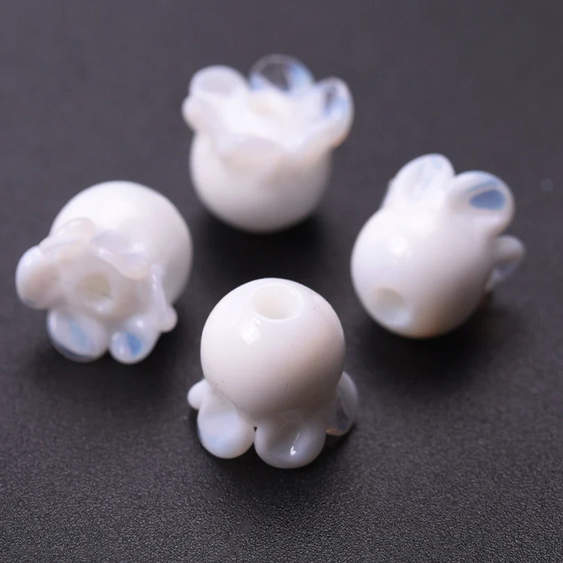 Several small, translucent white glass charm pendants shaped like lily of the valley buds are scattered on a dark surface.