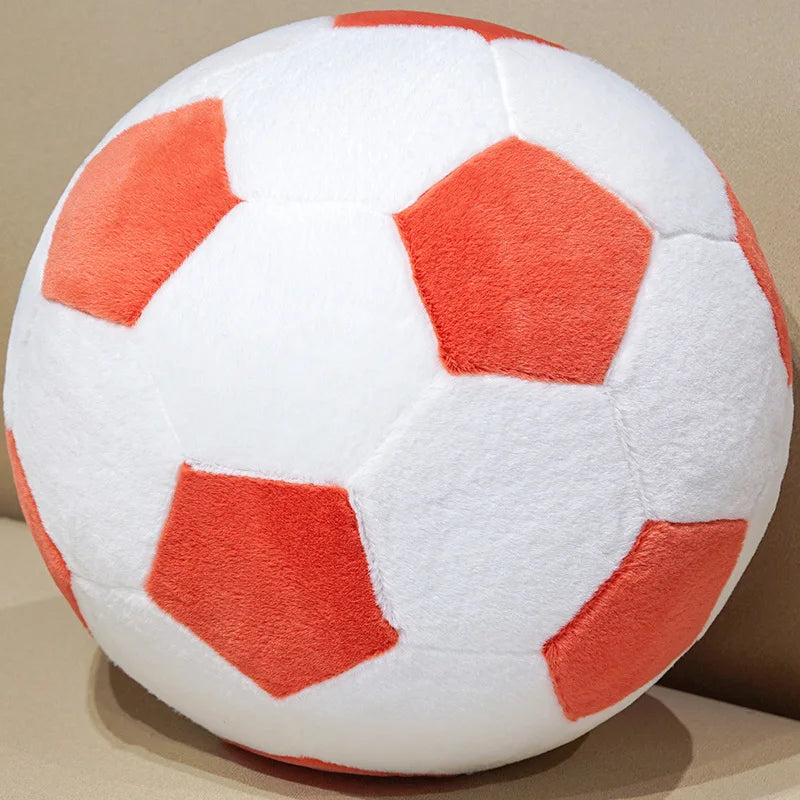 A white football plush pillow with orange pentagonal panels is shown in a close-up view.