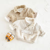 A beige toddler fleece-lined winter coat with a half-zip closure and light-colored sherpa trim, lying on a white surface.