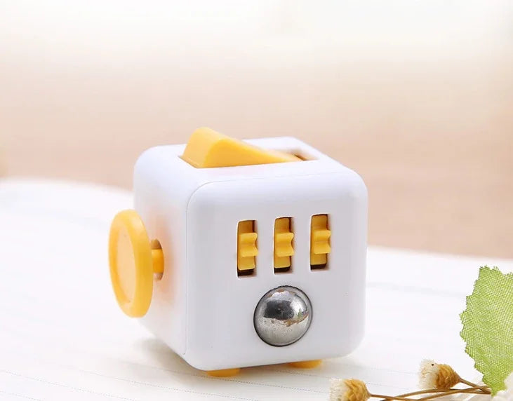 A white fidget cube with a rotating joystick, magnetic buttons, and a silver sphere on a wooden surface.