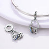 A silver heart charm with multicolored stones is displayed on a silver chain and next to a separate pendant.