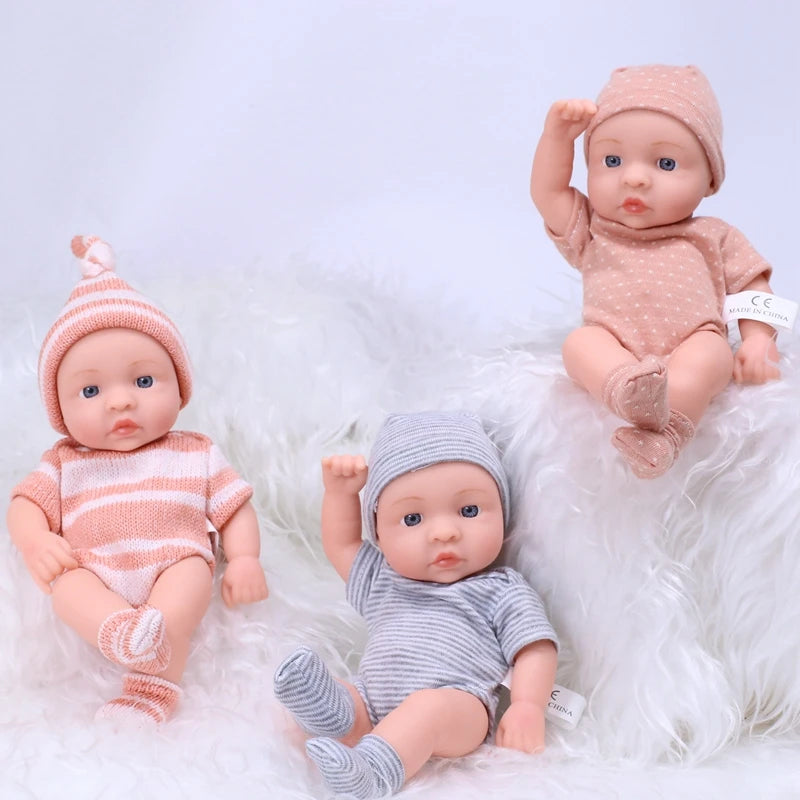 A collection of realistic soft vinyl reborn baby dolls dressed in pink and gray clothing sitting on white fluffy material.
