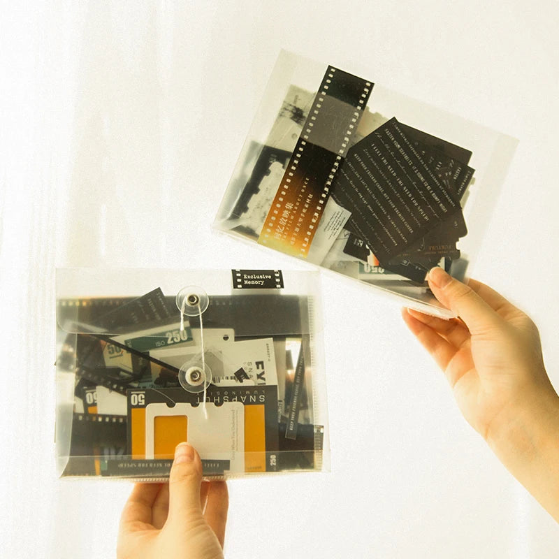 A hand holds a clear sheet containing various black and gold scrapbook stickers and paper for DIY crafts.